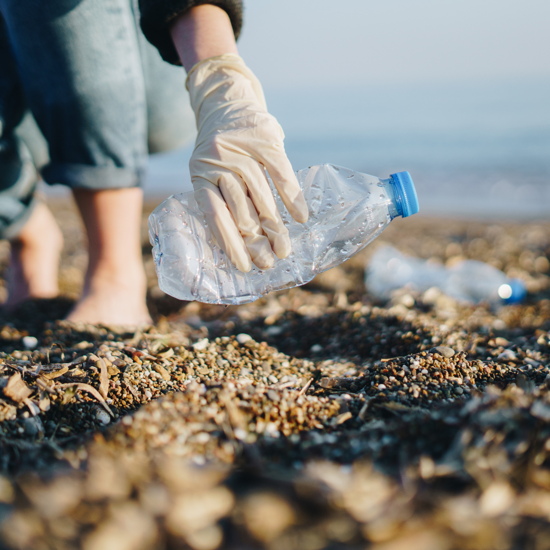 A picture of a person picking up a plastic water bottle on the sand. 