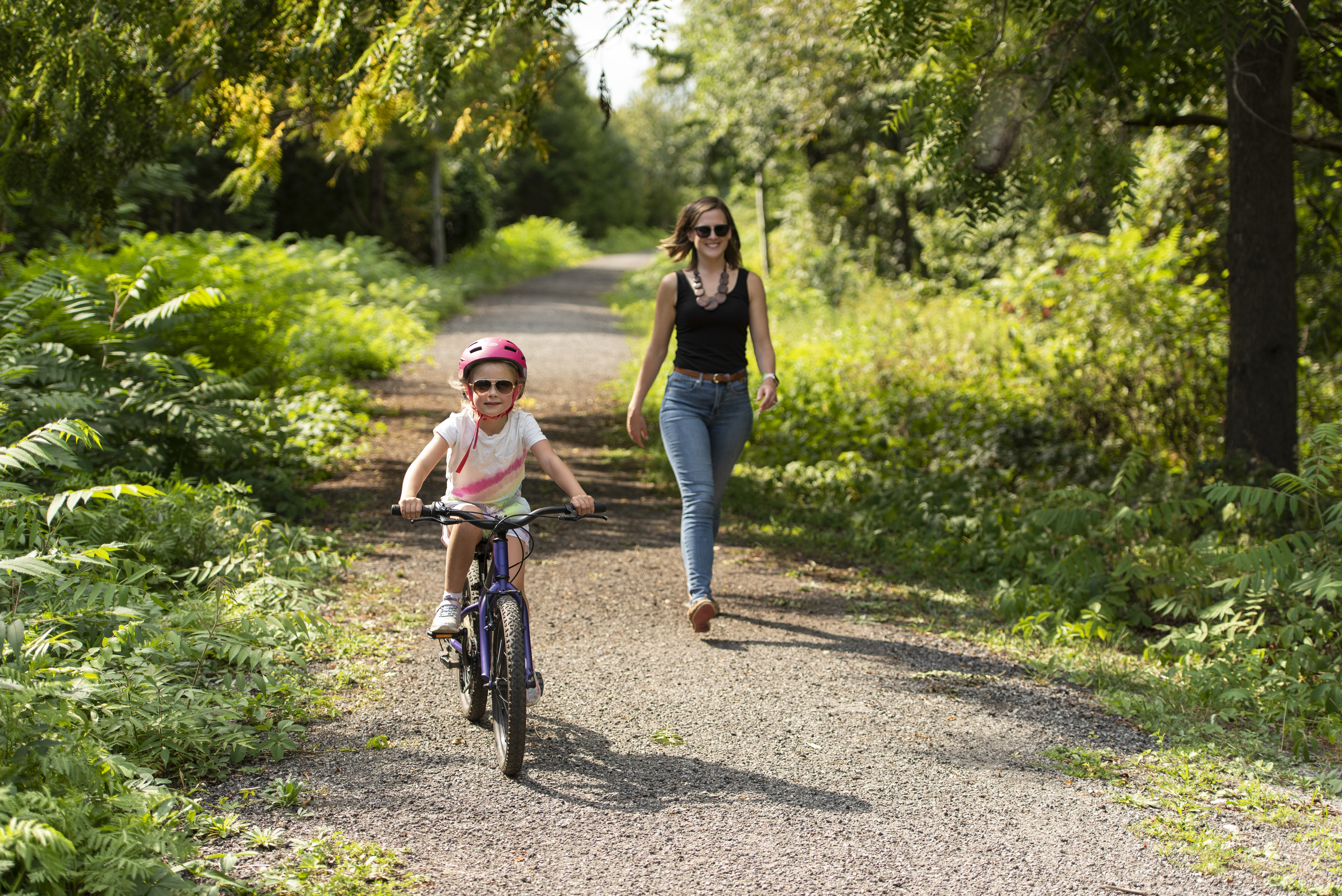 Image of a girl riding her bicycle with a person walking behind her