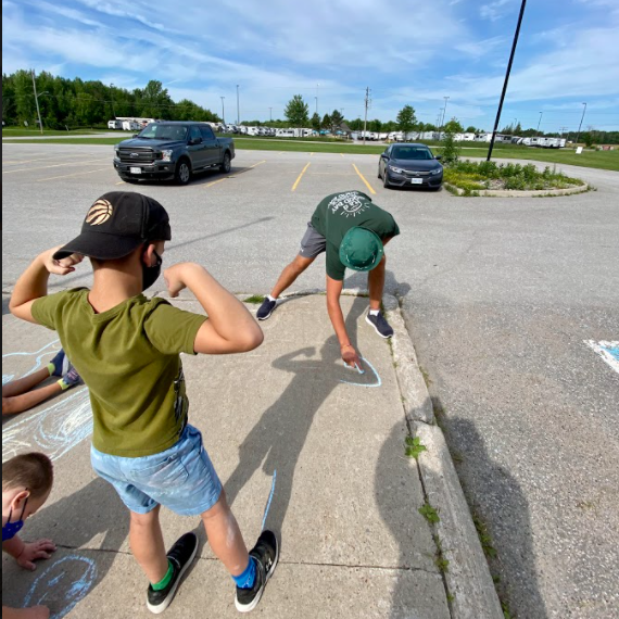 young boy showing muscles and and a volunteer tracing his shadow with chalk on the sidewalk 