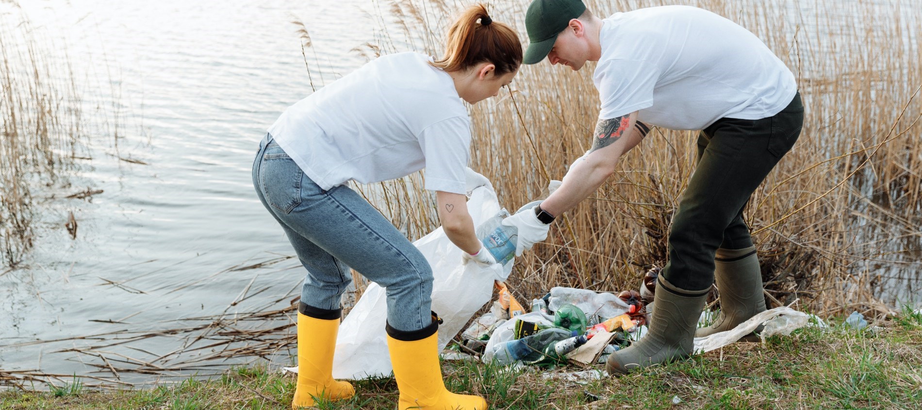 Picture of a man and a woman picking up garbage beside a body of water.