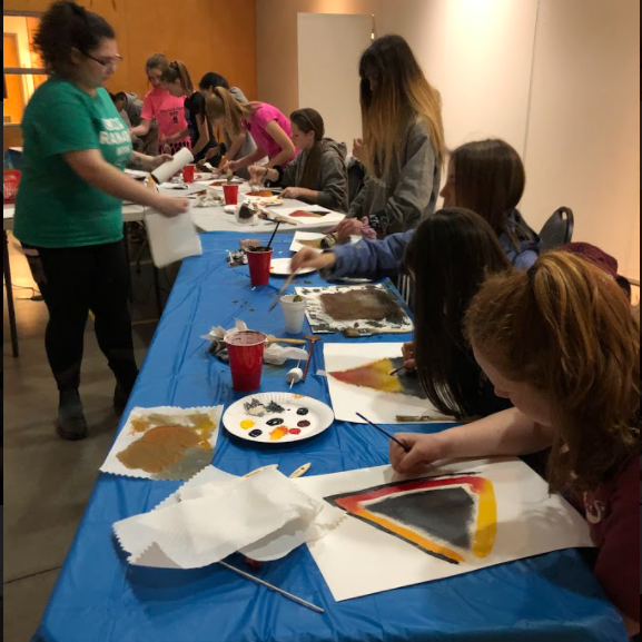 group of teens painting on a table with a blue table cloth