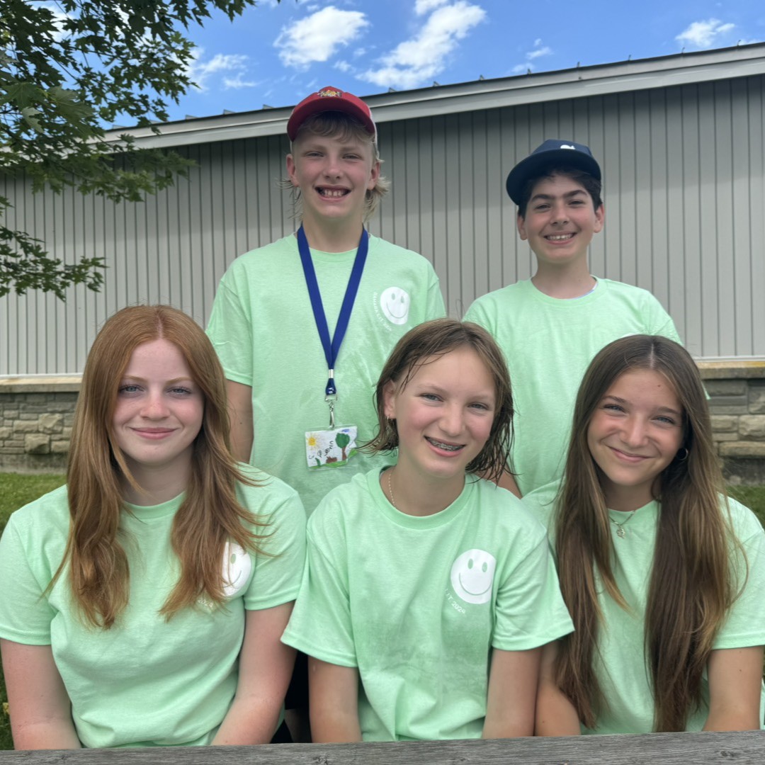 group of youth wearing matching green t shirts sitting at a table smiling