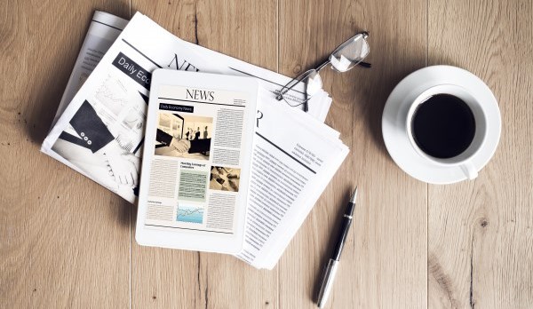 A picture of a newspaper, coffee and a pen on a table