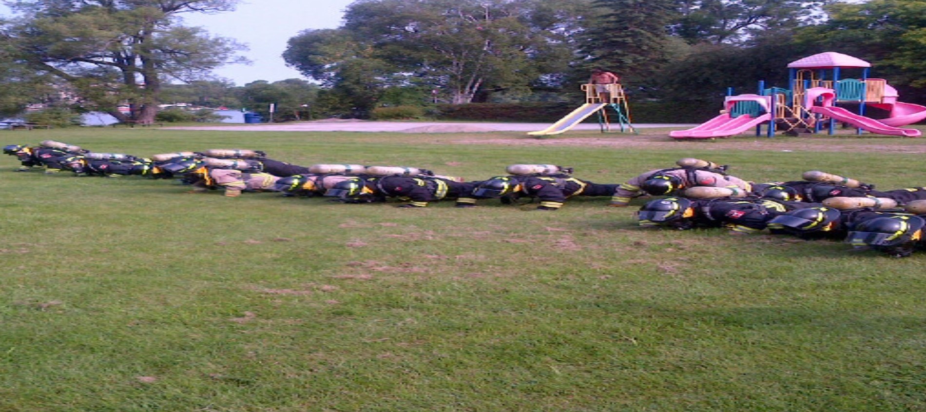 Fire fighters doing push ups in a park