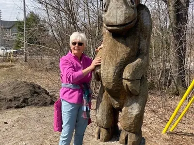 Photo of woman named Annalynn Faulkner standing with a large wood carving